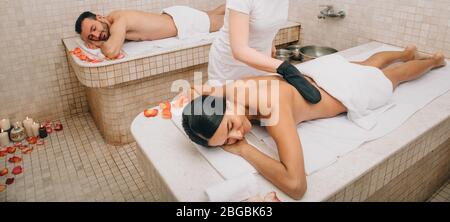 Gemischtes Rennpaar, das sich in einem türkischen Hammam Haut Peeling gibt. KESSA Handschuh Peeling im türkischen Bad Stockfoto