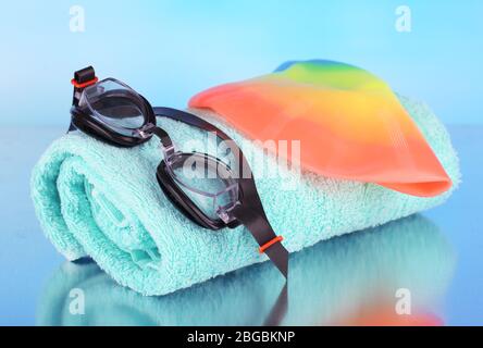 Set für Pool: Schwimmkappe, Schutzbrille und Handtuch auf blauem Hintergrund Stockfoto