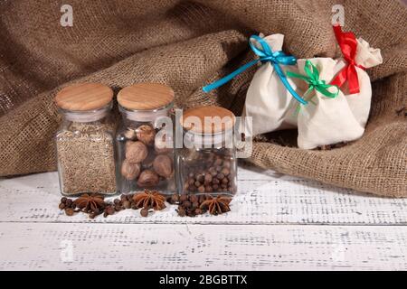 Säcke und Gläser voll mit Gewürzen, auf Holztisch, auf Sacktuch Hintergrund Stockfoto