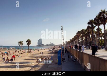 Blick auf viele Menschen, die sich auf Sand legen, sich sonnen und am berühmten Strand 'La Barceloneta' in Barcelona spazieren gehen. Es ist ein sonniger Sommertag Stockfoto