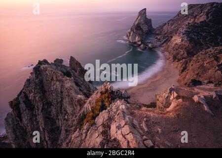 Reise nach Praia da Ursa Beach, Sintra, Portugal. Landschaftsaufnahme in fliederfarbenem, epischem Sonnenuntergangslicht. Scharfe Klippen und surreale Küsten des Atlantischen Ozeans. Stockfoto