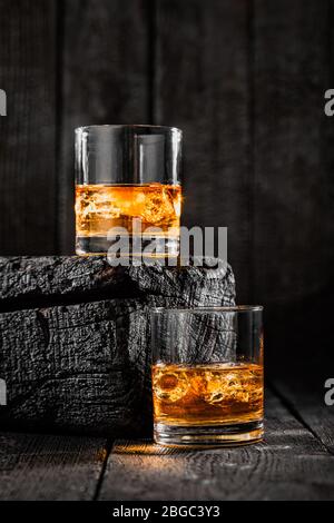 Zwei Gläser Whisky mit Eis auf verbranntem Holz Stockfoto