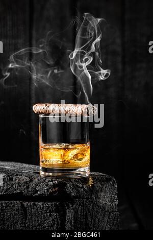 Zigarre auf einem Glas Whisky mit Eis rauchen Stockfoto