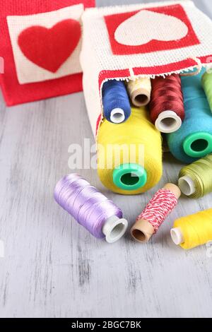 Taschen mit Spulen aus bunten Faden und Wollkugeln auf Holzhintergrund Stockfoto