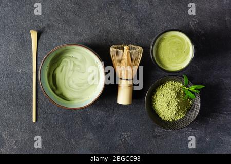 Bio-grüner Matcha-Tee. Matcha-Pulver und Matcha-Tee in einer Schüssel. Chashaku Löffel und Chasen Bambus Schneebesen für das Brühen Matcha Tee Draufsicht auf schwarzen Rücken Stockfoto