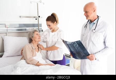Medizinische Betreuung von Senioren. Älterer Patient, der in einem Krankenhausbett liegt und eine Schwesternunterstützung hat. Klinische Behandlung und Altenpflege Stockfoto