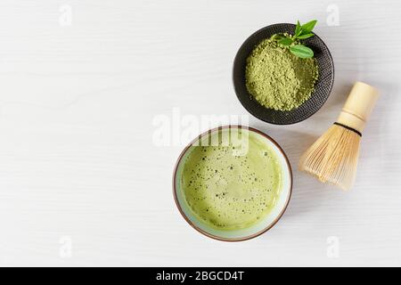 Bio-grüner Matcha-Tee. Matcha-Pulver und Matcha-Tee-Getränk in einer Schüssel. Chasen Bambus Schneebesen für das Brühen Matcha Tee Draufsicht auf weißem Holz Hintergrund Stockfoto