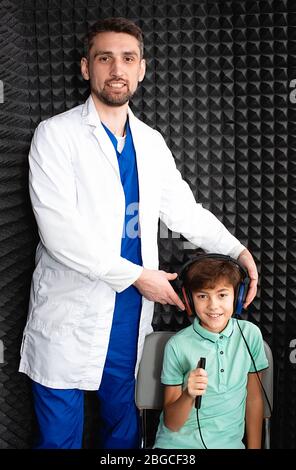 Positive kleine gemischte Rasse Junge mit Kopfhörern mit Hören exam.audiometry Test.Audiologe setzen Kopfhörer auf den Kopf des Kindes Stockfoto
