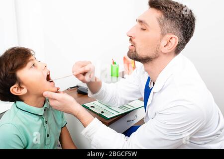 Kinderarzt überprüft die Kehle eines Jungen. Tonsillitis, Entzündung der Mandeln, Kind mit offenem Mund Stockfoto