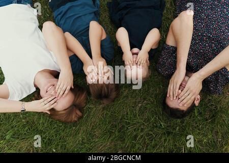 Junge Familie von vier Mitgliedern auf dem Gras liegen Augen mit Händen bedecken, schaffen Erinnerungen für ein Leben lang Stockfoto