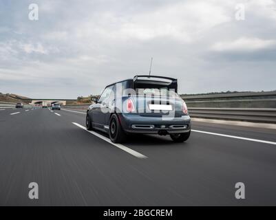 Blaues Mini-Cabriolet auf der Autobahn an einem bewölkten Tag im Hochland, Blick von hinten Stockfoto