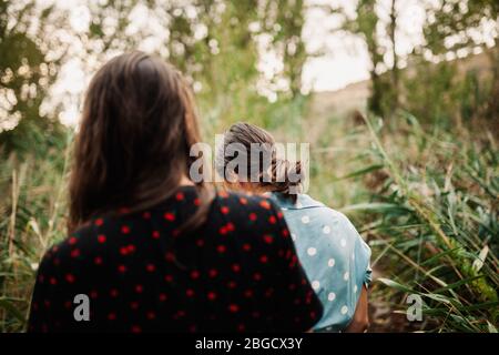 Rückansicht von zwei jungen Frauen, die in Kleidern und Turnschuhen durch das Feld gehen Stockfoto