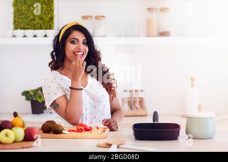 Schöne junge Frau bereitet Essen, beißen ein Gemüse während des Kochens Stockfoto