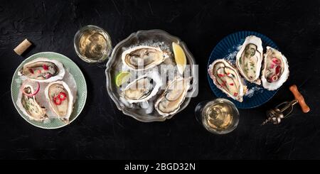 Austern mit verschiedenen Belägen Panorama, aufgenommen von oben mit Wein, mit Zitrone und Limette, Pfeffer, Zwiebel, auf dunklem Hintergrund Stockfoto