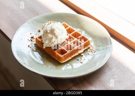 Hausgemachte klassische Waffeltörbe mit einer Kugel Vanilleeis. Topping mit Crush Mandel und Ahornsirup. Serviert in Keramikplatte. Stockfoto