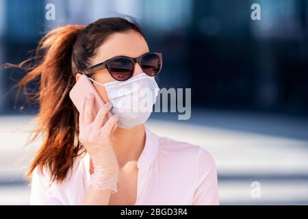 Nahaufnahme einer selbstbewussten Frau, die während coro vor dem Business Center läuft und eine Gesichtsmaske trägt und mit jemandem auf ihrem Mobiltelefon spricht Stockfoto