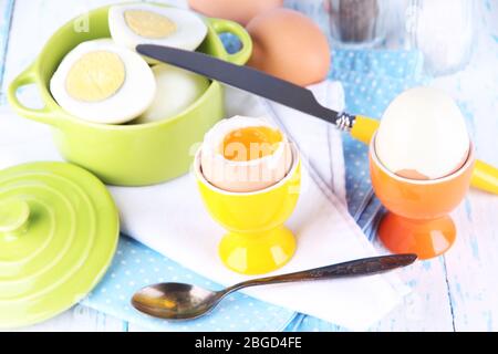 Gekochte Eier in Pfanne und Eierbecher auf farbigen Holzhintergrund Stockfoto