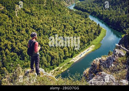 Ein Tourist mit Rucksack und Kamera auf einem Felsen und Blick auf das Flusstal Stockfoto