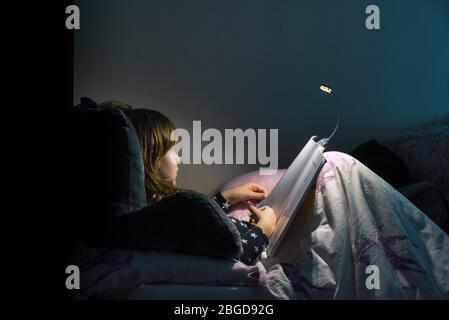 Mädchen liest ein Buch im Bett in der Nacht im komfortablen Schlafzimmer tragen Schlafanzug Stockfoto