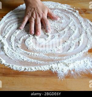 Kochkonzept. Frauenhand gießt Weizenmehl auf Holztisch. Start Kochen Pizza, Brot. Draufsicht. Stockfoto