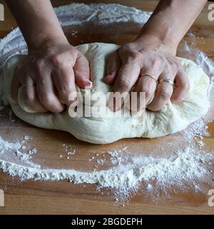 Kochkonzept. Weibliche Hände bereiten frischen hausgemachten Pizzateig auf bemehlten Holzbrett. Nahaufnahme. Italienische Küche. Stockfoto