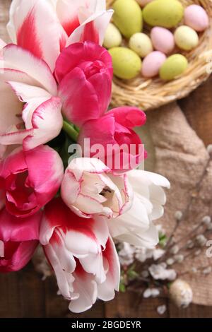 Komposition mit Ostereiern und schönen Tulpen in Glaskrug auf Holzhintergrund Stockfoto