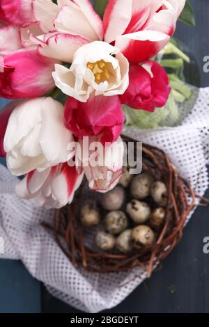 Komposition mit Ostereiern und schönen Tulpen in Glaskrug auf farbigem Holzhintergrund Stockfoto