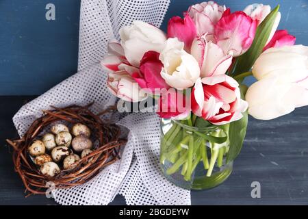 Komposition mit Ostereiern und schönen Tulpen in Glaskrug auf farbigem Holzhintergrund Stockfoto