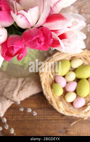 Komposition mit Ostereiern und schönen Tulpen in Glaskrug auf Holzhintergrund Stockfoto