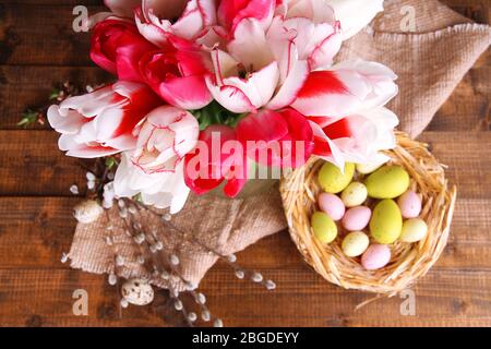 Komposition mit Ostereiern und schönen Tulpen in Glaskrug auf Holzhintergrund Stockfoto