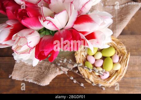Komposition mit Ostereiern und schönen Tulpen in Glaskrug auf Holzhintergrund Stockfoto