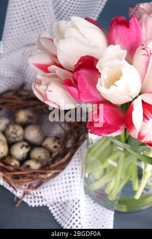Komposition mit Ostereiern und schönen Tulpen in Glaskrug auf farbigem Holzhintergrund Stockfoto