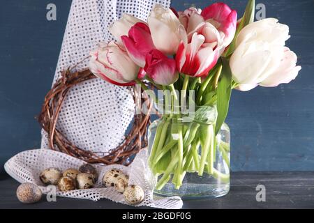Komposition mit Ostereiern und schönen Tulpen in Glaskrug auf farbigem Holzhintergrund Stockfoto
