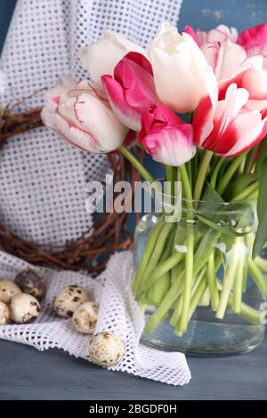Komposition mit Ostereiern und schönen Tulpen in Glaskrug auf farbigem Holzhintergrund Stockfoto
