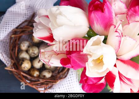 Komposition mit Ostereiern und schönen Tulpen in Glaskrug auf farbigem Holzhintergrund Stockfoto