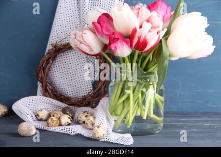 Komposition mit Ostereiern und schönen Tulpen in Glaskrug auf farbigem Holzhintergrund Stockfoto