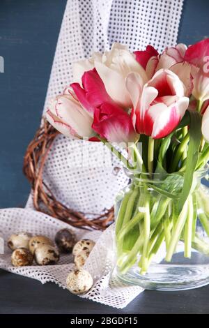 Komposition mit Ostereiern und schönen Tulpen in Glaskrug auf farbigem Holzhintergrund Stockfoto