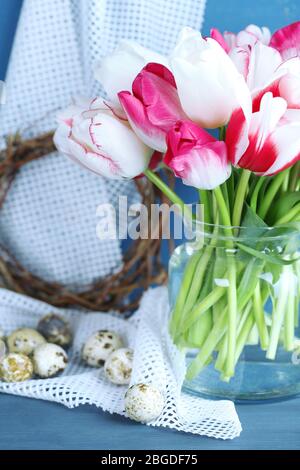 Komposition mit Ostereiern und schönen Tulpen in Glaskrug auf farbigem Holzhintergrund Stockfoto