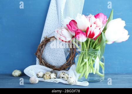 Komposition mit Ostereiern und schönen Tulpen in Glaskrug auf farbigem Holzhintergrund Stockfoto