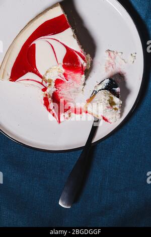Kreative minimalistische Food-Fotografie, Erdbeer Käsekuchen auf einem weißen Teller mit Löffel über dunkelblauem Hintergrund. Stockfoto