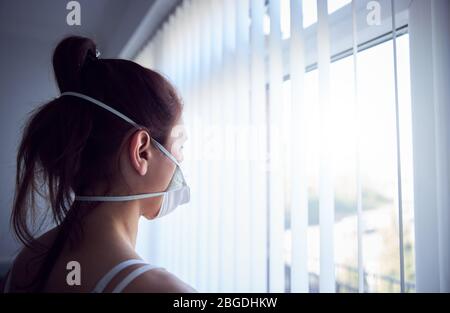 Junge Frau aus dem Fenster mit Schutzmaske Landschaftsaufnahme. Stockfoto
