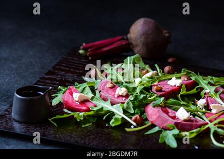 Frischer Salat aus Rote Bete, Käse und Rucola auf schwarzem Holzhintergrund Stockfoto