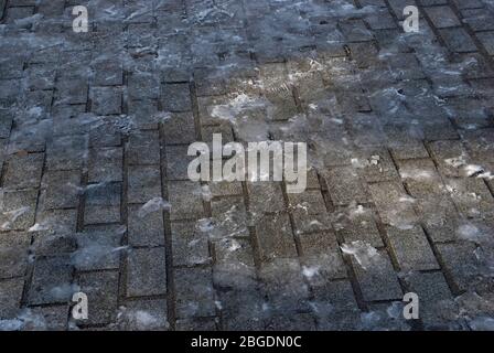Straßenblock Pflaster im Winter mit einer dünnen Schicht aus Eis und Fußspuren und einem kleinen Pool von Licht Stockfoto