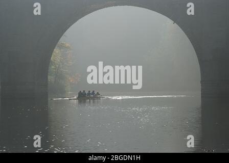 Ein Rennboot mit vier Crew und cox während des Übungruderns unter dem Bogen einer Steinbrücke am River Wear in Durham City während eines nebligen Herbsttages Stockfoto