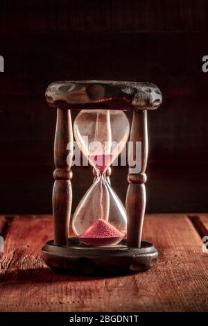 Das Konzept der Zeit läuft aus. Eine Sanduhr mit durchfallendem Sand, auf einem dunklen rustikalen Hintergrund Stockfoto