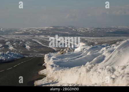 Straße über die Moore an der Grenze Weardale - Teesdale in der Grafschaft Durham im Winter mit Schnee, der nach dem Pflügen hoch am Straßenrand aufgehäuft wird Stockfoto