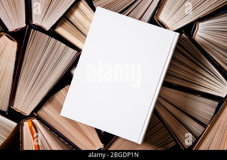 Weißes Buch in weißem Einband mit Platz für Text liegt auf bunten alten offenen Büchern Stockfoto