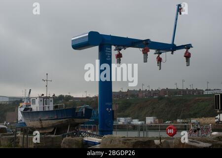 Statischer Stromkran am Seaham Hafen mit erhöhtem Kleinboot am Hafen und Reihenhaus der Stadt im Hintergrund Stockfoto