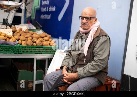 Älterer Mann sitzt neben einer Kiste mit Kartoffeln auf der Electric Avenue, Brixton, London Stockfoto