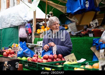 Eine ältere Verkäuferin, die neben ihren Obst-Produkten auf der Electric Avenue, Brixton, London, sitzt Stockfoto